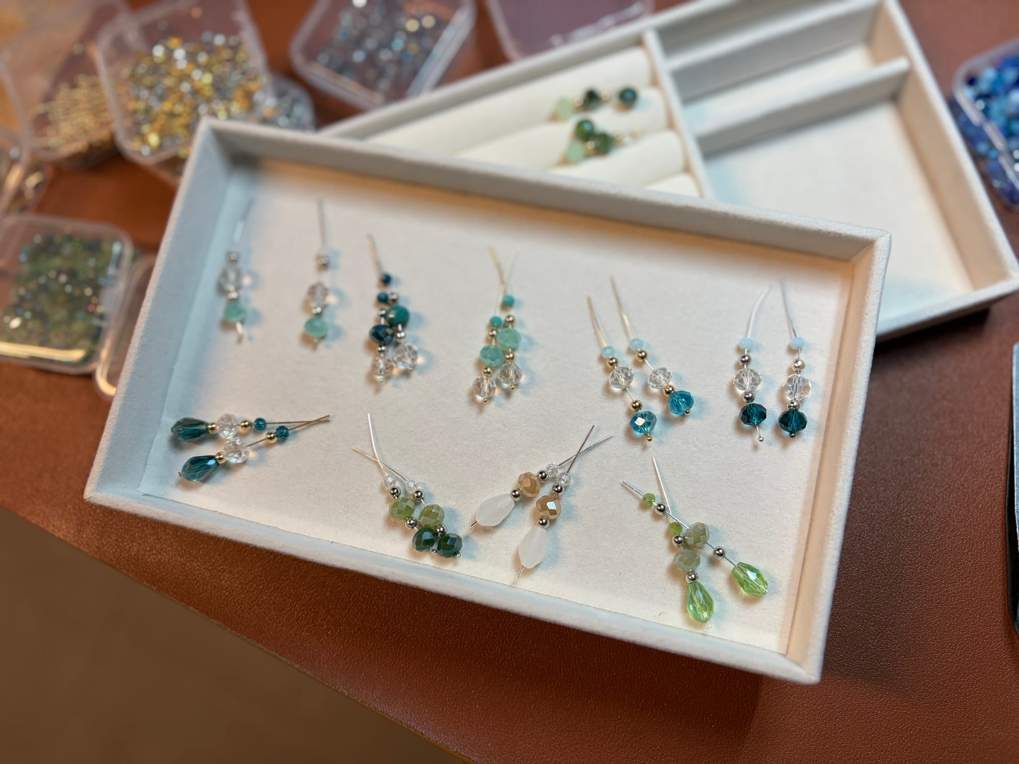 Un plateau blanc rectangulaire et les paires montées posées dessus, entouré de boîtes de perles colorées